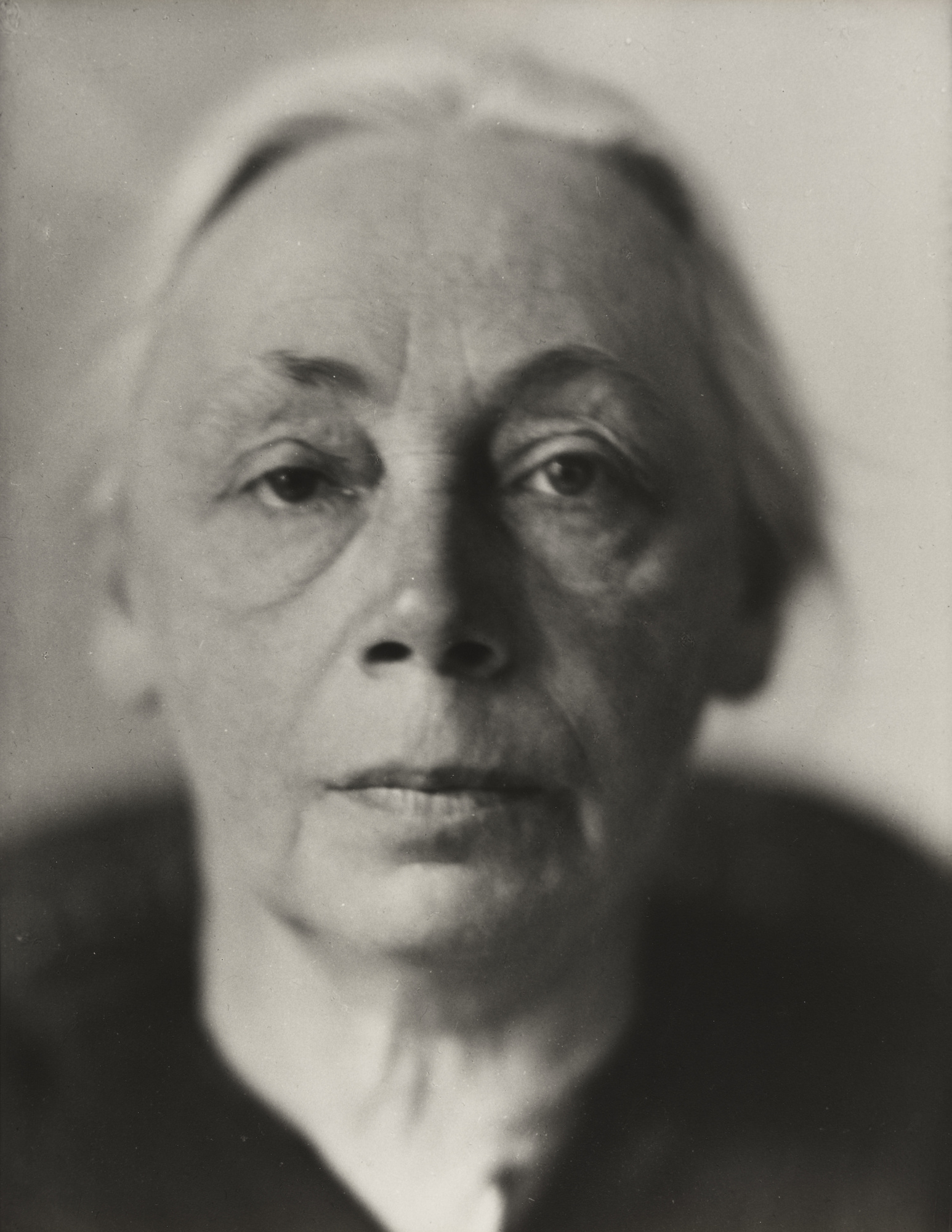 Black and white portrait of an elderly person with a neutral expression. The close-up highlights aged skin and wispy hair, evoking a sense of wisdom. Käthe Kollwitz.