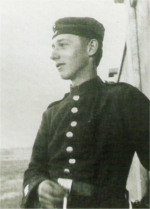 A young soldier in early military uniform stands outside, gazing into the distance. The image is black and white, evoking a historical, contemplative mood. Peter Kollwitz in uniform.