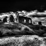 A dramatic black and white image of the ancient stone ruins of Castell Dinas Brân under a cloudy sky. The scene conveys a sense of mystery and timelessness.