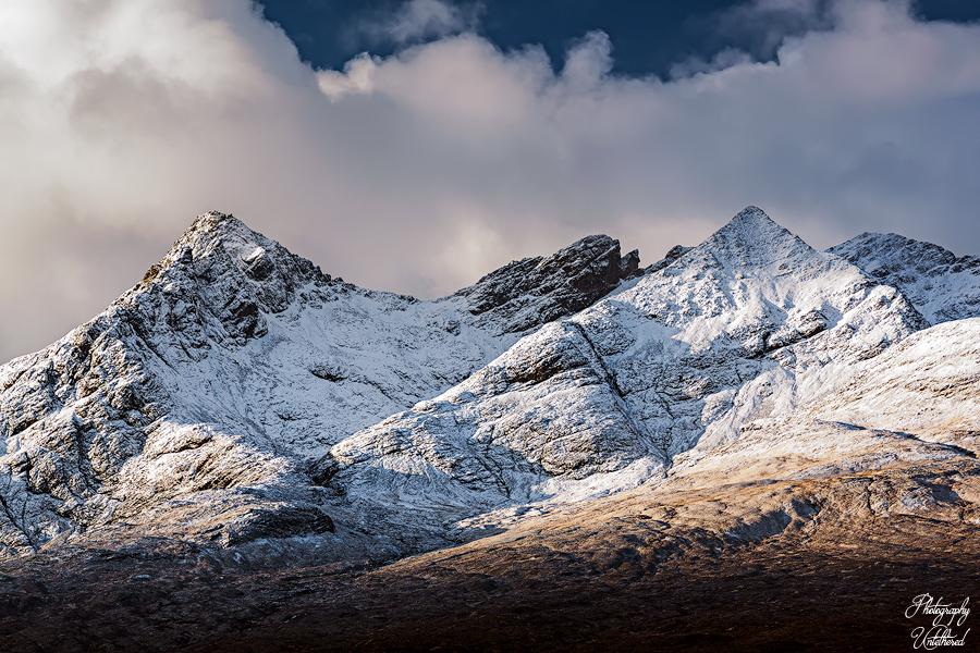 A majestic snow-covered mountain rises against a clear blue sky, showcasing its rugged peaks and winter landscape. Sgùrr nan Gillean: Isle of Skye. 