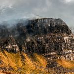 Rugged mountain landscape with dramatic cliffs shrouded in mist, contrasting the golden-brown grassy slopes below. Moody, atmospheric scene. An Stòr Skye.
